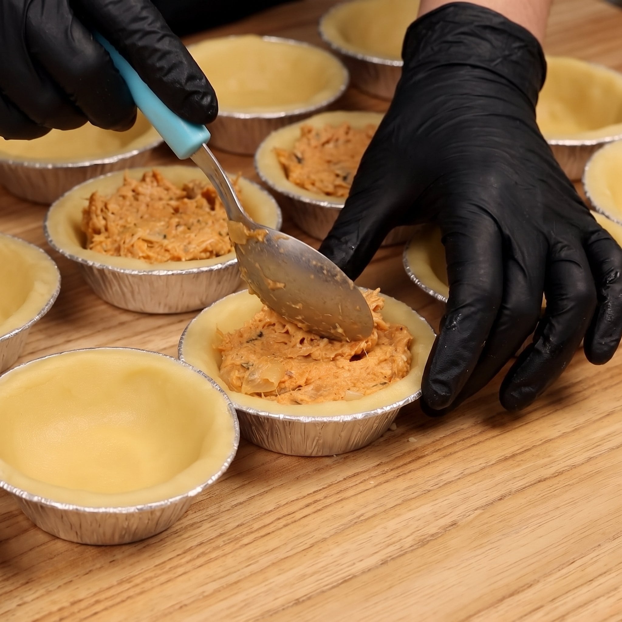 Mãos de luva recheando as forminhas de empada com frango